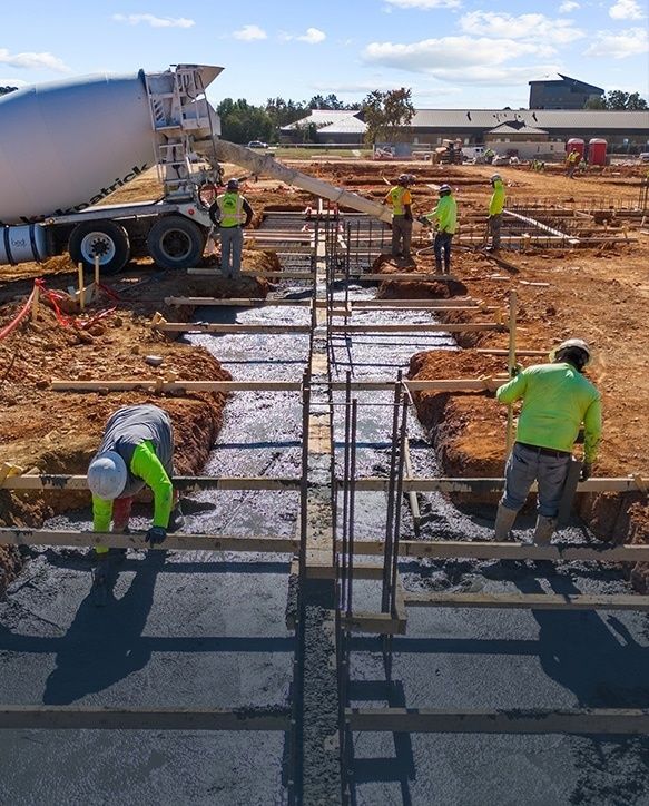 Arbeiter gießen Beton in eine bewehrte Fundamentkonstruktion für eine Stahlhalle