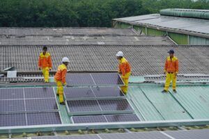 Vier Arbeiter montieren Solarmodule auf einem Hallendach