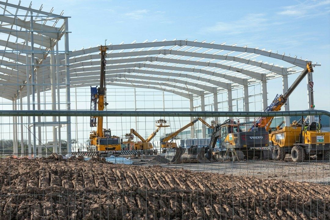 Baustelle einer großen Stahlhalle mit Kränen und Baufahrzeugen